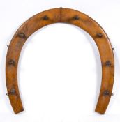 An early 20th century oak horseshoe shaped riding crop or gun rack:, with eight pegs, 74cm wide.