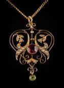 An Edwardian 9ct gold garnet, peridot and seed pearl pendant: of open scroll design,