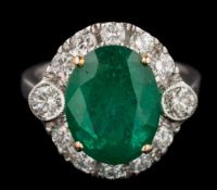 An emerald and diamond oval cluster ring: the central oval emerald approximately 12.5mm long x 9.