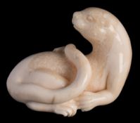 A carved fossilised marine ivory model of a sea otter: with raised head and curved tail, 8cm. long.