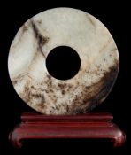 A Chinese jade bi-disc: of plain design with pierced centre and wood stand, 9cm. diameter.