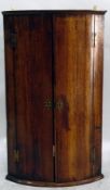 Georgian oak bowfront corner cupboard, the pair of panelled doors enclosing shelves,