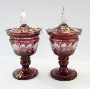 Pair of Victorian cranberry glass pedestal lidded urns with clear glass finials, rose etched
