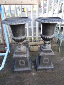 A pair of dark grey painted cast iron garden urns on laurel wreath decorated stands (outside)