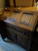 A dark oak linen fold-style drop front bureau with single drawer above a two cupboard / drawer base