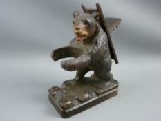 A CARVED BLACK FOREST BEAR TAPER HOLDER & MATCHBOX STAND formed as a standing bear, arms