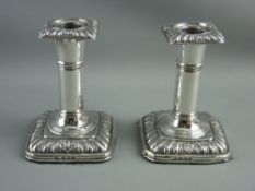 A PAIR OF SQUARE BASED SHORT STEMMED SILVER CANDLEHOLDERS with plain columns and feather edged
