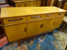 A GOOD G-PLAN TEAK LONG SIDEBOARD of three drawers and four cupboard doors, all with carved