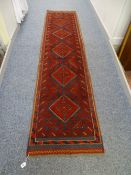 A HAND KNOTTED WOOL MESHWANI RUNNER CARPET, predominantly red ground with central repeating