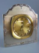 A SILVER CLOCK STAND with inset Tecnis alarm clock insert, the stand with shaped top with engine