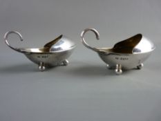 A PAIR OF EGG SHAPED CREAM JUGS having curled handles and covered pouring aperture on three ball