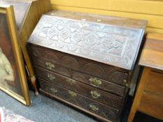 An antique oak drop down bureau with profuse carving & brass fittings