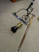 Comical metal sculpture of a man riding a penny farthing, a trophy and a tomahawk shaped walking