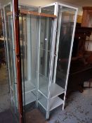Two modern narrow standing glass shelved display cabinets