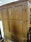 A large three-door honey pine wardrobe on a two-drawer base, 198 x 157 x 58cms