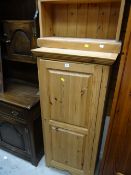 A tall narrow pine cupboard together with a pine open bookcase