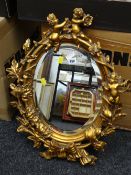 A small oval bevel glass mirror with gilt wood surround decorated with cherubs & leaves