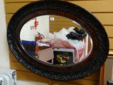 A large oval bevelled glass mirror in a heavy wooden frame