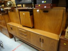 A large G-Plan style teak lounge unit with drop front cupboards above cupboards either end to a