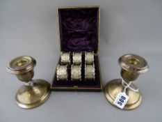 Pair of Chester silver squat candlesticks (damages) and a cased set of six white metal napkin rings
