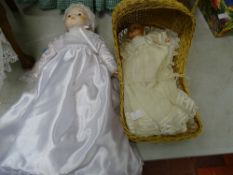 Baby doll with silk dress and bonnet and a miniature baby doll with cream dress in a straw crib