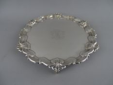 A CIRCULAR SILVER SALVER on three knurled feet with wavy border and central monogram, Sheffield