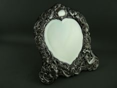 A SILVER FRAMED EASEL HEART SHAPED MIRROR, the bevelled glass having a finely shaped and decorated