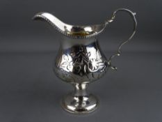 A CLASSICALLY STYLED SILVER PEDESTAL CREAM JUG with embossed floral decoration and gilt interior,