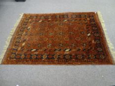 AN EASTERN STYLE TUFTED WOOL CARPET, rust ground with repeating central pattern and multi-bordered
