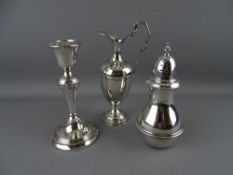 A SILVER SUGAR SIFTER, a single candlestick and a small ewer type jug both having loaded bases,