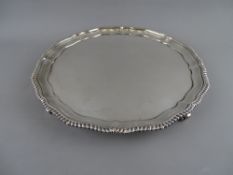 A LARGE CIRCULAR SILVER SALVER with wavy edge and gadrooned border on four gripping hand feet,