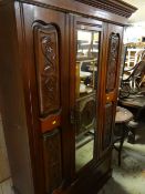 An Edwardian stained wood single-mirror door wardrobe with carved decoration to side panels above