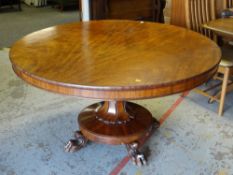 A large nineteenth century mahogany tilt-top dining table with a carved pedestal on lion claw feet