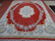 A CHINESE WASHED WOOLLEN CARPET, predominantly red ground with central floral motif and bordered