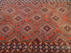 AN EASTERN STYLE CARPET, predominantly red ground with central repeating diamond pattern and