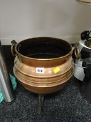A copper coal bucket with copper handles standing on three feet