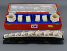 Small Indian carved ivory elephant train and a set of six cased Eastern napkin rings with peacock