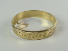 A 9CT GOLD LADIES SCROLL & FOLIATE ENGRAVED BANGLE, 15.9grams approx.