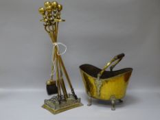 A SET OF VICTORIAN BRASS FIRE IRONS on a stand with a vintage brass coal scuttle on four claw feet