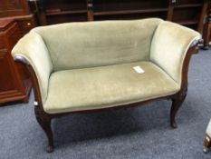 An antique carved mahogany settee in green upholstery with scroll arms, 130cms wide