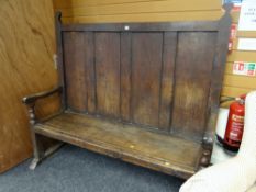 An antique oak settle having a four-panel back & with single plank seat on turned & block