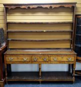 An antique oak Welsh dresser having a planked platform base, three drawers, an open rack with carved