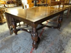 A 1930s stained oak draw leaf stretcher table on pineapple cup supports & with curved stretcher