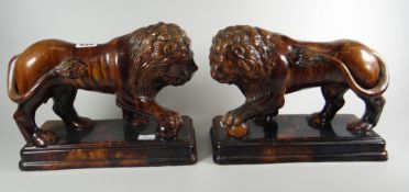 A pair of Rockingham or style treacle glazed standing empire-lions on rectangular stepped bases