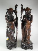 PAIR OF CARVED HARDWOOD FIGURES OF CHINESE ELDERS OR OFFICIALS holding staffs raised on naturalistic