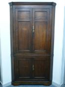 A GEORGE III OAK FLOORSTANDING CORNER CUPBOARD having double panel twin upper doors and original