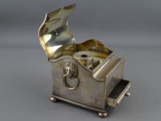 AN ELECTROPLATED SINGLE BOTTLE DESK STAND of casket form with shaped lid and pen aperture, lion mask