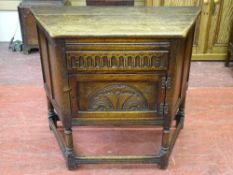 A REPRODUCTION OAK SINGLE DOOR SIDE CABINET with carved front detail on turned and block supports,
