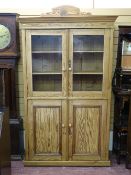 A VINTAGE STRIPPED PINE HOUSEKEEPER'S CUPBOARD with twin glazed upper doors and interior shelving