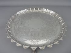A CIRCULAR SILVER TRAY with chased decoration and raised pierced pattern border, on four scrolled